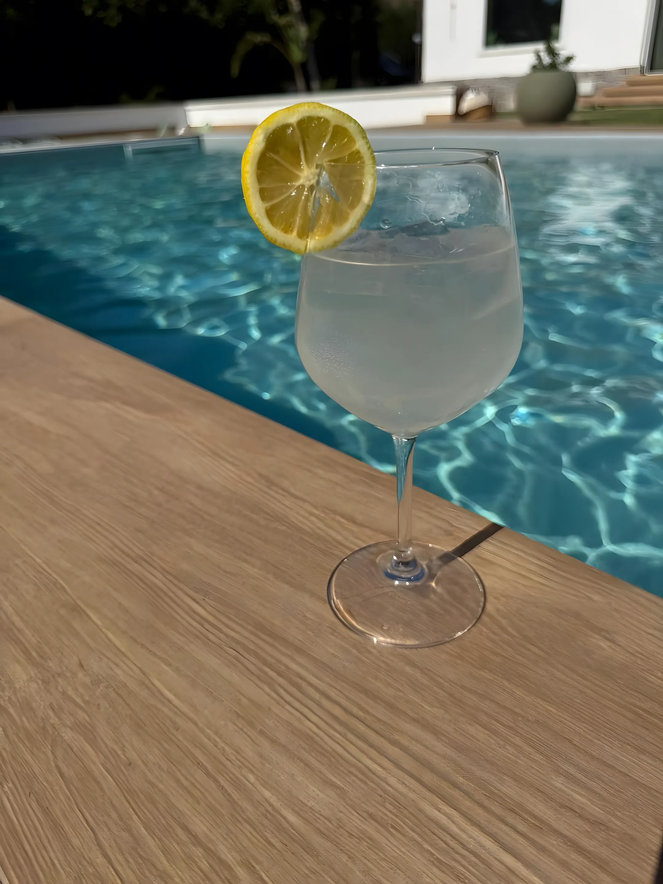 Calice di spritz al limone sul bordo piscina in legno