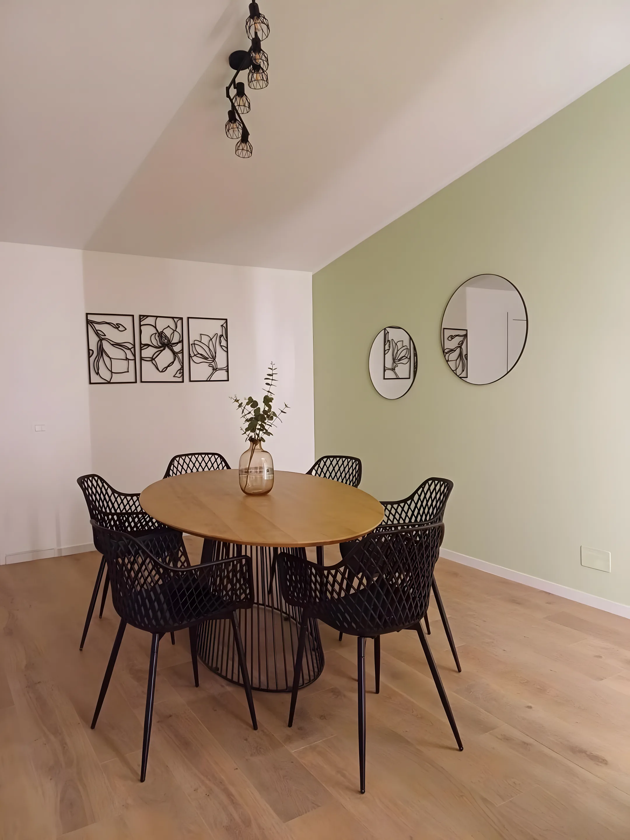 Sala da pranzo con tavolo rotondo, parete verde e specchi tondi